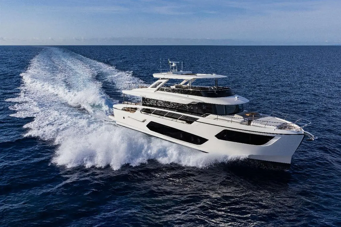 A sleek white yacht glides through blue waters, creating splashes and wake under a clear sky.